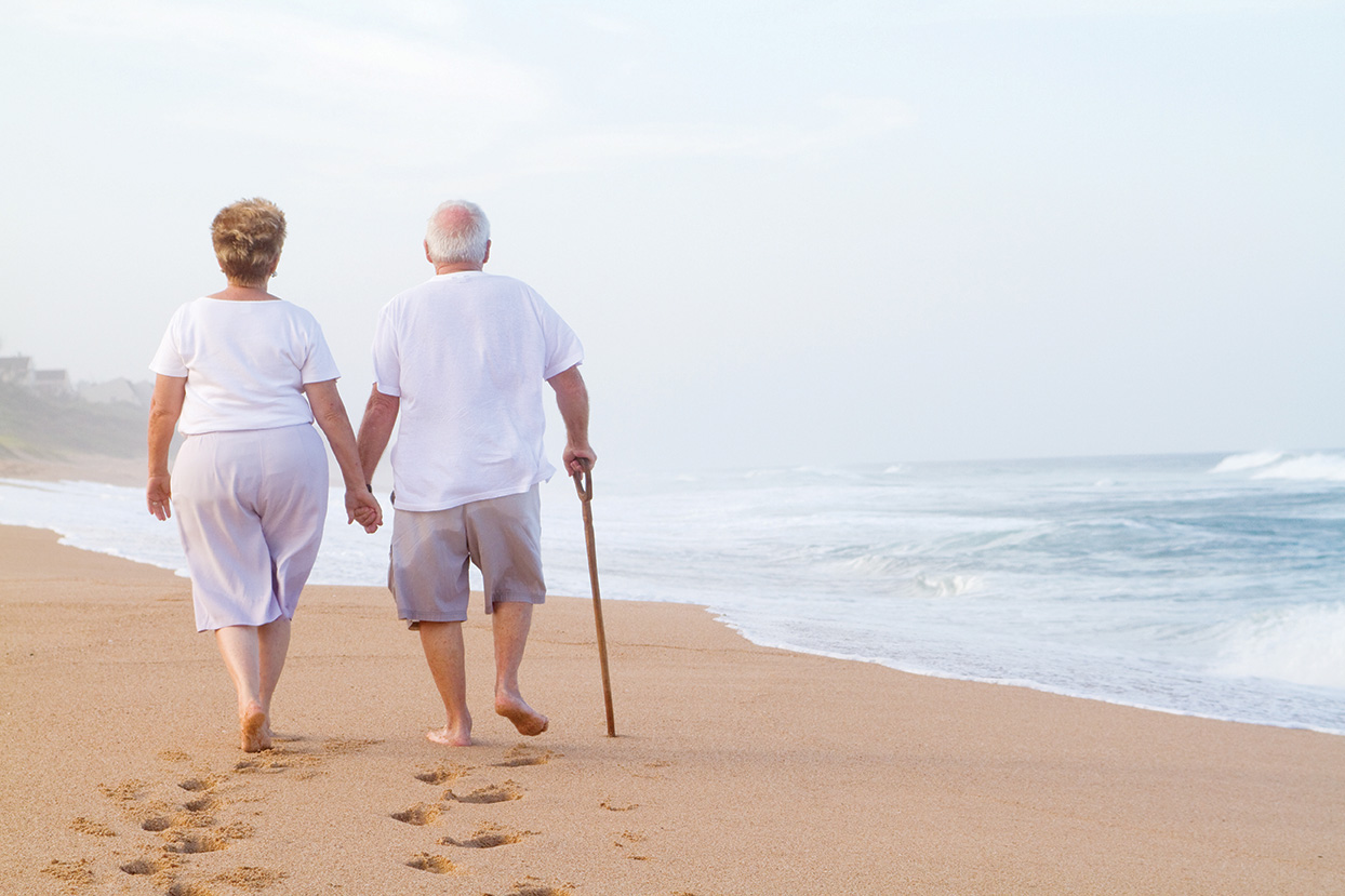 senior couple hand in hand walking on beach